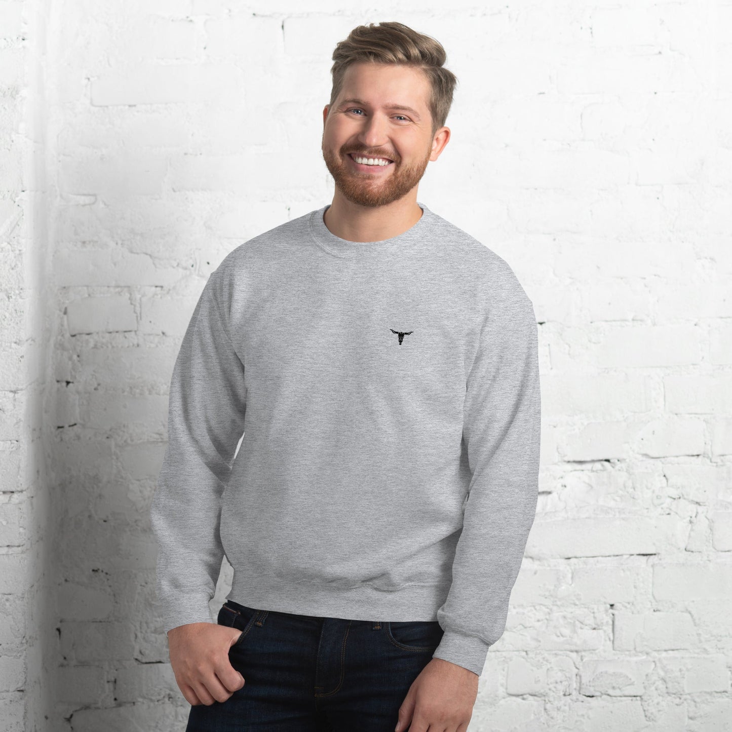 Man wearing grey Bull Skull Unisex Sweatshirt with small black bull skull logo on chest