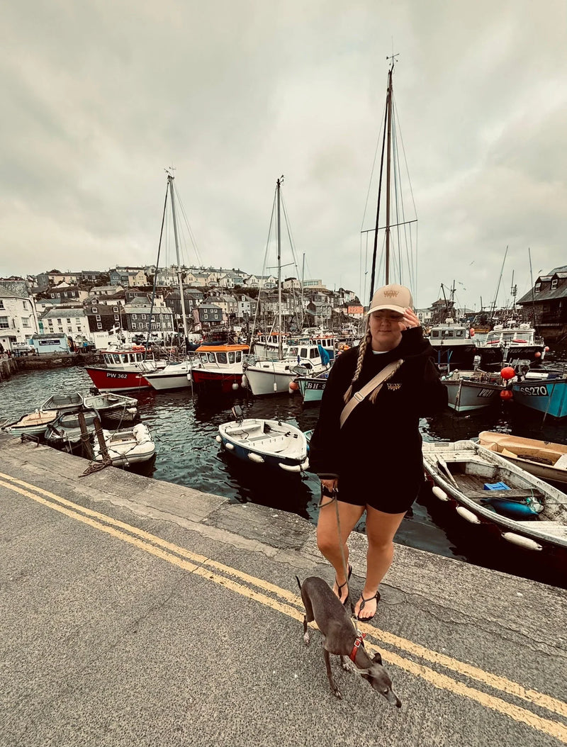 Woman with a small dog on a harbor dock, fishing boats and hillside village in background
