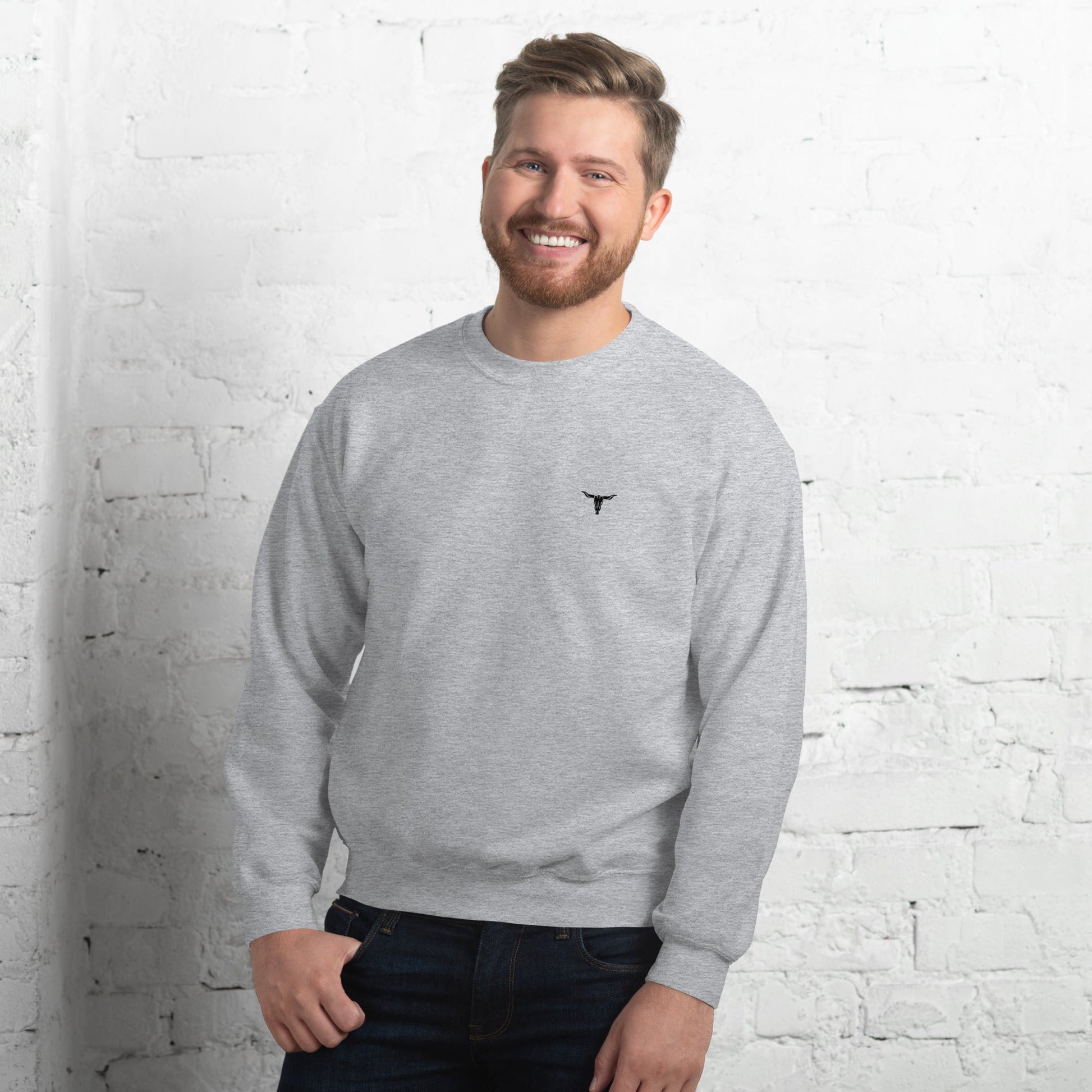 Man wearing grey Bull Skull Unisex Sweatshirt with small black bull skull logo on chest